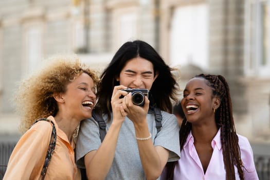 Three women are laughing and taking a picture together. One of them is holding a camera. Scene is happy and lighthearted