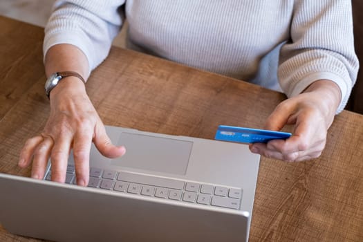A cheerful mature woman is making an online purchase or payment, utilizing a credit card and a laptop computer. Online banking concept.