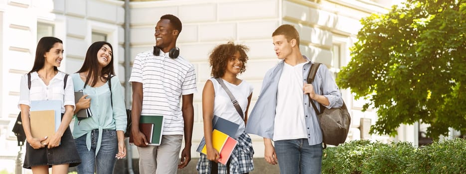 Campus Life. Group of international students walking outdoors after classes, holding workbooks, chatting together and smiling