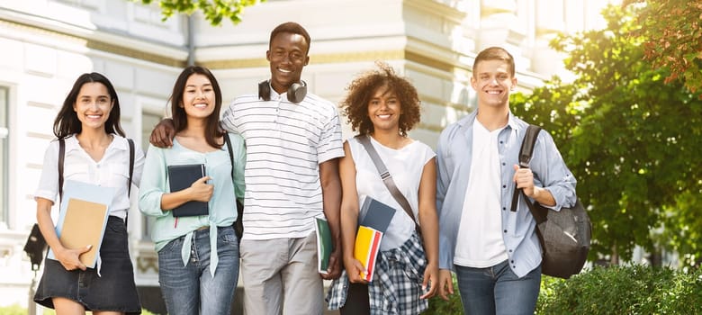 Portrait of happy international college students walking together in campus after classes, free space