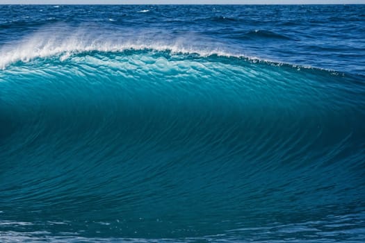 This captivating image captures the raw power and beauty of a large wave in the ocean as it crests and breaks, forming a curved hollow tube. The spray of white foam on top adds to its dramatic effect.