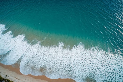 This captivating aerial image showcases the serene beauty of a sandy beach with the ocean's waves gently rolling onto the shore. The breaking waves create a white, frothy pattern along the water's edge, adding a touch of dynamic energy to the tranquil scene.