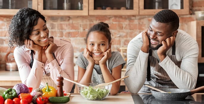 Happy afro family cooking healthy dinner together at kitchen, posing at camera, making salad, panorama with copy space