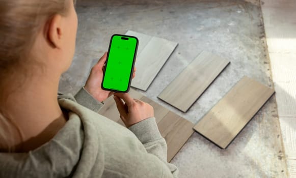 Interior designer Holding Device with Green Chroma Key Screen above Luxury Vinyl Wood Samples, Laminate On Floor In House. Choosing, Selecting Waterproof Flooring. Home Reconstruction. Horizontal