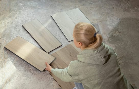 Woman Holds Luxury Vinyl Wood Samples On Concrete Floor In House. Choosing, Selecting Waterproof Flooring. Home Reconstruction. Vinyl Tiles Collection, Patterns. Interior Design Idea. Horizontal