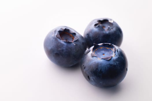 Blueberries on a white background. Three blueberries lie on the table, close-up.
