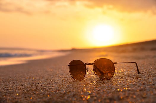 Mirrored sunglasses lie on a sandy beach. Close-up of sunglasses, beautiful trendy sunglasses located on the floor of the beach and blurred sea background.