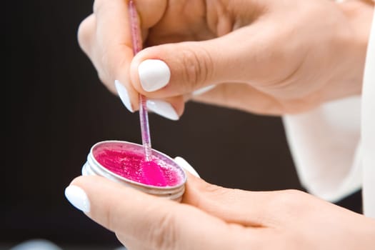 Close-up of woman's hands with a tube of eyebrow gel or eyebrow soap. Professional eyebrow lamination procedure in a beauty salon. Beauty care concept.