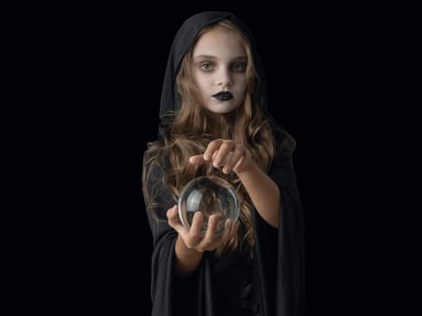 Little girl in Halloween witch costume and dark make-up holding crystal ball isolated on white background