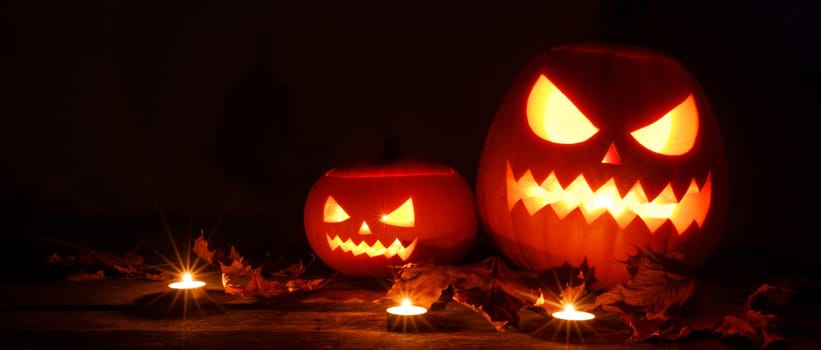 Three glowing Halloween Pumpkin lanterns and burning candles on dark wooden background