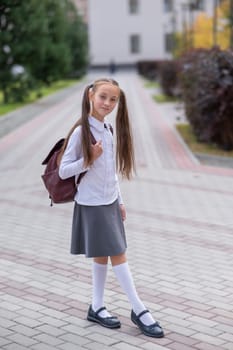 Caucasian girl in uniform and with a backpack goes from school