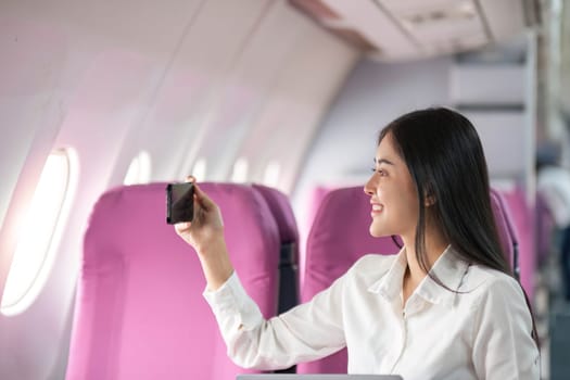 Smiling tourist woman taking a selfie on her mobile phone waiting on the plane. Passengers traveling abroad during the weekend air flight concept.