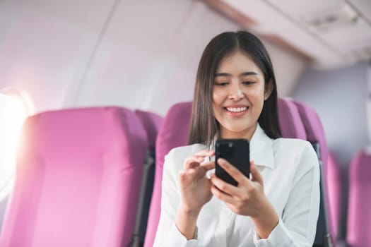 Smiling tourist woman taking a selfie on her mobile phone waiting on the plane. Passengers traveling abroad during the weekend air flight concept.