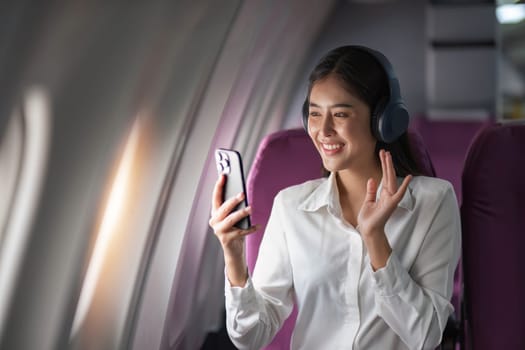 Asian woman sitting and using a smartphone in an airplane Listening to music next to the airplane seat window travel and technology concept.