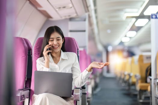 Asian woman using modern smartphone and laptop computer while sitting on airplane Asian woman sitting next to airplane seat window travel and technology.