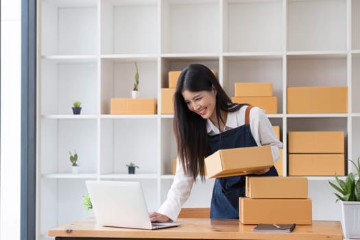 Portrait business woman smile and use laptop checking information on parcel shipping box before send to customer. Entrepreneur small business working at home. SME business online marketing..