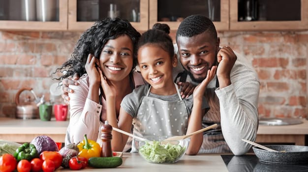 Lovely black family cooking healthy dinner together at kitchen, posing at camera, making salad, panorama with copy space