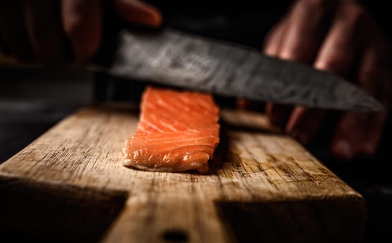 Chief hands cut salmon fillet with knife on wooden table closeup view. Red fish steak for healthy seafood dinner