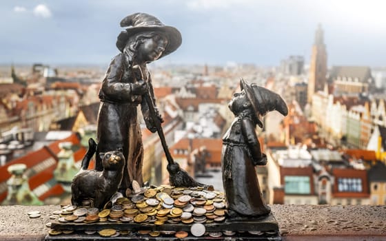 Famous dwarf gnome sculpture in Wroclaw with coins against amazing Wroclaw city view. Money tradition and monument in Poland.
