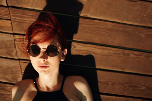 Top view portrait of redhair woman lying on wooden jetty at a lake during her restorative holiday.