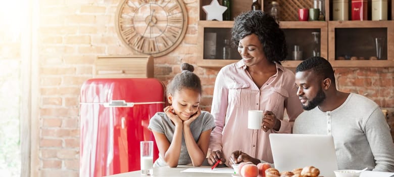 Young afro family having weekend breakfast together at home, using laptop, drawing, free space