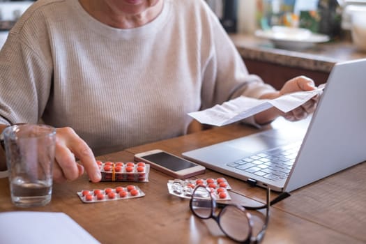 Hand of senior woman holding leaflet to prescribed medicine, pills lying beside on table. Closeup patient reading information sheet.