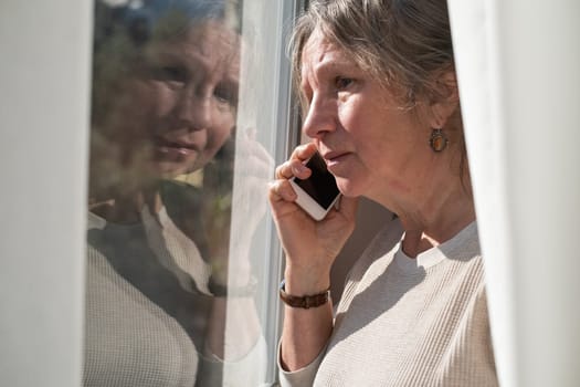 Important message. Serious aged latin female pensioner stand by picture window at home hold phone