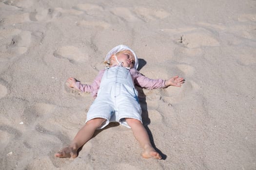 Little girl on sand and playing at sea beach in warm sunny summer day