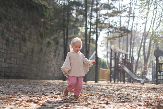 autumn outdoor portrait of beautiful happy child girl walking in park playing with leaves