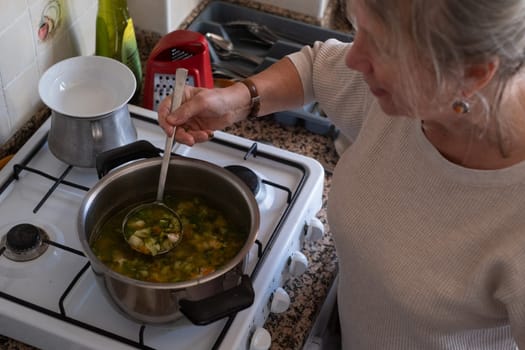 Senior old eldery aged woman grandmother cooking soup in kitchen at home. Grandma preparing food, meal. Healthy food, vegetarian concept. Dieting and healthy lifestyle.