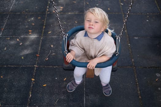 Cute smiling kid girl playing on a swing outdoor on a playground. Children summer activity.