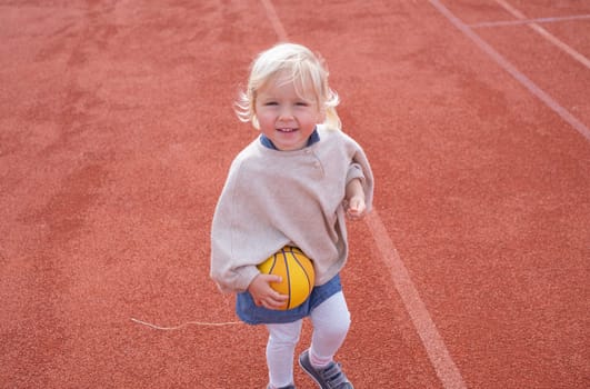 The caucasian child is playing with the ball on a playground