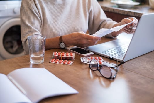 Hand of senior woman holding instruction to prescribed medicine, pills lying beside on table. Closeup patient reading information sheet.