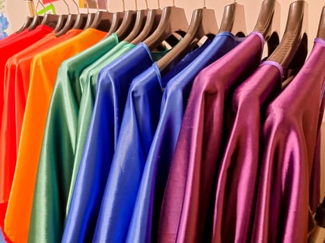Rainbow colors. Choice of casual clothes on wooden hangers, isolated on white.