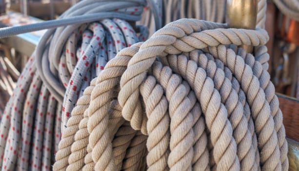 Maritime scene featuring a neatly coiled thick rope and another blurred rope with red specks in background, probably used on a ship. High quality photo