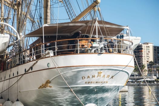 Danish traditional tall ship 'Danmark' docked at urban harbor. Features include multiple masts, complex rigging and portholes, suggesting usage for education or tourism. High quality photo