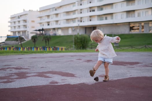 Little girl playing with a cone as it is a ball. Toys from nature