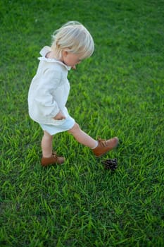 Little girl playing with a cone as it is a ball. Toys from nature