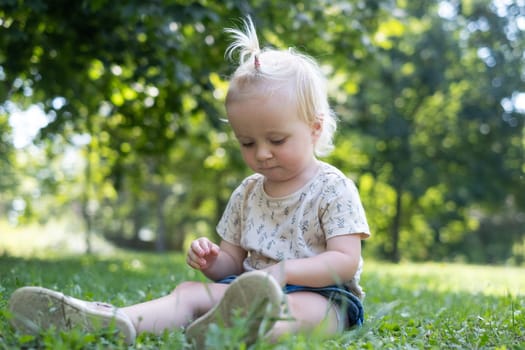 Funny baby kid outside. Cute adorable baby girl in yellow dress sitting on grass in park outdoors.