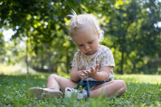 Funny baby kid outside. Cute adorable baby girl in yellow dress sitting on grass in park outdoors.