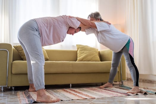 Senior woman exercising at home together with daughter. Active mature woman doing stretching exercise in living room at home.