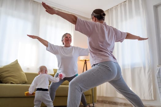 Senior woman exercising at home together with daughter. Active mature woman doing stretching exercise in living room at home.