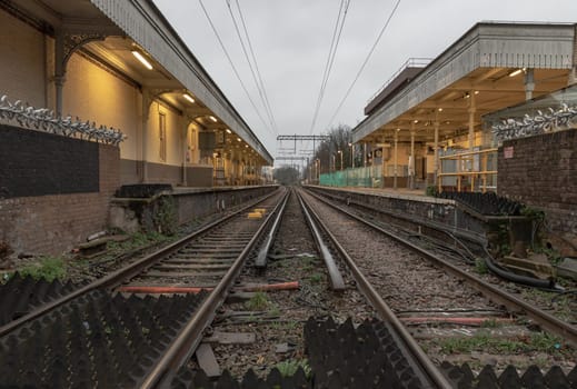London, UK - Dec 25, 2023 - Perspective view on empty railway tracks and electric infrastructure equipment, wires at Acton central rail station. The Railway system with Metal frames of Train platform, Transport and shipping landscape concept, Railroad track rails, Train tracks, Railway station, Space for text, Selective focus.
