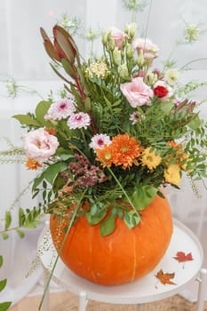 Flower arrangement in a pumpkin, autumn interior decor. Creating handmade autumn decor