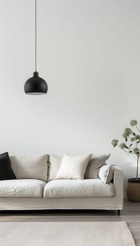 A white sofa with plush pillows sits in a bright, minimalist interior, illuminated by a black pendant light hanging from the ceiling.