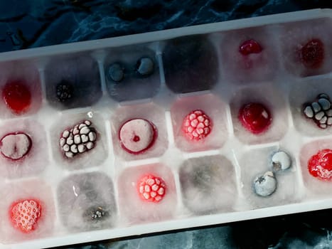 Frozen ice with berries in a container by the piece for making refreshing drinks or preserving vitamins and minerals seasonal cherries, raspberries, strawberries, blackberries, mulberries, blueberries