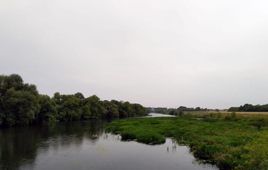 A scenic view of a calm river winding through a lush green landscape under a cloudy sky.