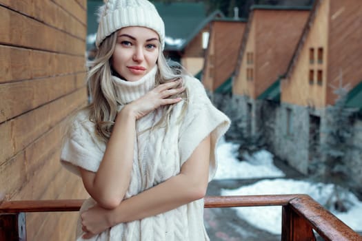 Portrait of a beautiful girl in a white hat and sweater on the street on the balcony. Warm winter clothes.