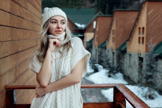 Portrait of a beautiful girl in a white hat and sweater on the street on the balcony. Warm winter clothes.