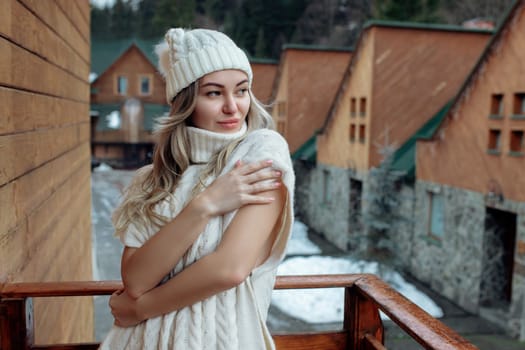 Portrait of a beautiful girl in a white hat and sweater on the street on the balcony. Warm winter clothes.